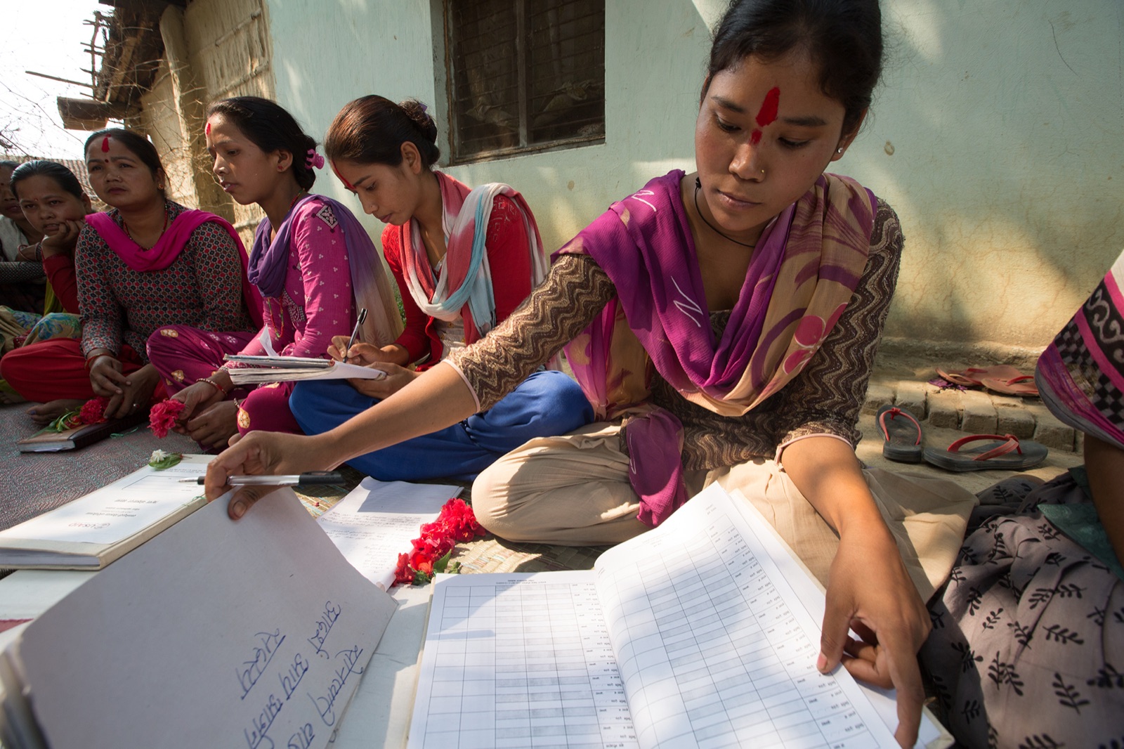 Members of a WORTH savings group recording transactions by hand in a paper ledger before digitisation